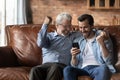 Excited two generations of men celebrating success, using smartphone Royalty Free Stock Photo