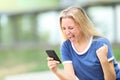 Excited winner teenage girl celebrating news on phone in a park