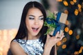 Excited woman in Christmas night sitting near tree and lifting her Christmas gift to listen what`s inside Royalty Free Stock Photo