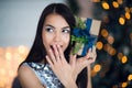 Excited woman in Christmas night sitting near tree and lifting her Christmas gift to listen what`s inside Royalty Free Stock Photo