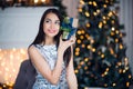 Excited woman in Christmas night sitting near tree and lifting her Christmas gift to listen what`s inside Royalty Free Stock Photo