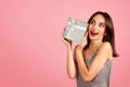 An excited woman with a gleeful expression, holding a glittery gift box with a white ribbon