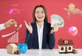 Excited woman with money and house models at table against background. Real estate agent Royalty Free Stock Photo