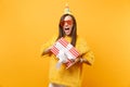 Excited woman in orange funny glasses, birthday hat holding red box with gift present celebrating and enjoying holiday