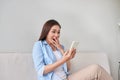 Excited woman reading text on a phone lying on a couch in the living room at home