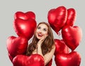 Excited woman with red heart balloons on white background. Happy surprised model girl with red lips makeup, long curly hair. Gift