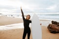 Excited woman surfer posing with her surfing board, enjoying water sport and smiling at camera, standing on the beach