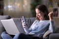 Excited woman using phone and laptop in the night