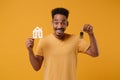 Excited young african american guy in casual t-shirt posing isolated on yellow orange background, studio portrait