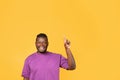 African guy with one arm raised pointing upwards, yellow backdrop Royalty Free Stock Photo