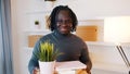 Excited young african american man moving in to the new apartment. Holding cardboard boxes with plant and books Royalty Free Stock Photo