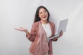 Excited young Asian business woman holding a laptop while pointing to the copy space beside her on isolated white background Royalty Free Stock Photo