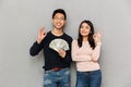 Excited young asian loving couple holding money showing okay gesture. Royalty Free Stock Photo