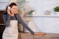 Excited young asian woman with headphones singing and dancing while dusting a wooden cabinet in living room.