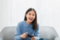 Excited young Asian woman sitting on sofa and holding joystick with playing games in the living room at home. Royalty Free Stock Photo