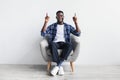 Excited young black man having idea and pointing two fingers up at empty space, sitting in armchair, mockup Royalty Free Stock Photo