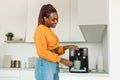 Excited young black woman making fresh aromatic coffee in modern machine in kitchen interior Royalty Free Stock Photo