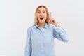 Excited young blonde woman pointing finger up, looking at camera with open mouth, have a cool idea, standing in blue shirt over Royalty Free Stock Photo