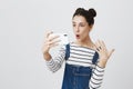 Excited young brunette woman making selfie using smart phone. Student girl with hairbuns in striped shirt taking