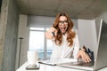 Excited young business woman dressed in formal clothes shirt indoors using laptop computer pointing to you