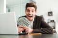 Excited young businessman showing money using laptop computer. Royalty Free Stock Photo