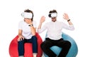 Excited young couple experiencing virtual reality seated on beanbags isolated on white background