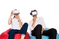 Excited young couple experiencing virtual reality seated on beanbags isolated on white background