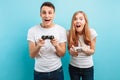 Excited young couple, a guy and a girl, with joysticks in their hands playing video games on a blue background