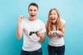 Excited young couple, a guy and a girl, with joysticks in their hands playing video games on a blue background