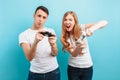 Excited young couple, a guy and a girl, with joysticks in their hands playing video games on a blue background