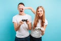 Excited young couple, a guy and a girl, with joysticks in their hands playing video games on a blue background