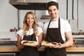 Excited young friends loving couple chefs on the kitchen holding plates with tasty food. Royalty Free Stock Photo