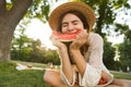 Excited young girl in summer hat having a picnic at the park, sitting on a grass, Royalty Free Stock Photo