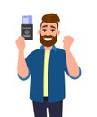 Excited young hipster man showing passport with tickets and gesturing raised hand fist. Happy bearded person holding boarding pass Royalty Free Stock Photo