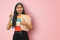 Excited young indian asian girl student posing islolated holding textbooks and pointing up with palms front, looking directly at