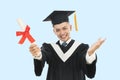 Excited young man in  black graduation gown and cap holding a diploma Royalty Free Stock Photo