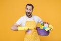 Excited young man househusband in apron rubber gloves doing housework isolated on yellow background. Housekeeping