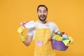 Excited young man househusband in apron rubber gloves hold basin with detergent bottles washing cleansers doing