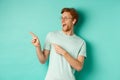 Excited young man with red hair, wearing glasses and t-shirt, pointing and looking left at awesome promotion, smiling