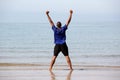 Excited young man standing on beach with arms outstretched Royalty Free Stock Photo