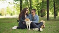 Excited young people loving couple are fussing cute dog shiba inu scratching its fur, talking and laughing sitting on