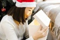 Excited young smiling asian woman in santa hat open xmas gift, magic fulfillment of desires at New Year or Christmas