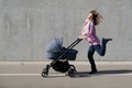 Excited young woman dancing while pushing newborn stroller by gray concrete wall. Ecstatic mother having fun while walking with Royalty Free Stock Photo