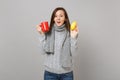 Excited young woman in gray sweater, scarf holding lemon and red cup of tea isolated on grey background. Healthy fashion Royalty Free Stock Photo