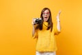 Excited young woman in heart eyeglasses spreading hand taking pictures on retro vintage photo camera isolated on bright Royalty Free Stock Photo