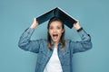 Excited young woman in jeans shirt holding computer or laptop over head in front of blue background. Royalty Free Stock Photo