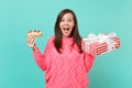 Excited young woman in knitted pink sweater hold eclair cake red striped present box with gift ribbon isolated on blue Royalty Free Stock Photo