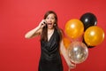 Excited young woman in little black dress holding air balloons, talking on mobile phone, screaming isolated on bright Royalty Free Stock Photo