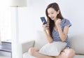 Excited young woman looking at her smart phone and smiling while sitting on the sofa at home Royalty Free Stock Photo