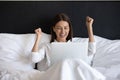 Excited young woman looking at laptop screen, relaxing in bed. Royalty Free Stock Photo